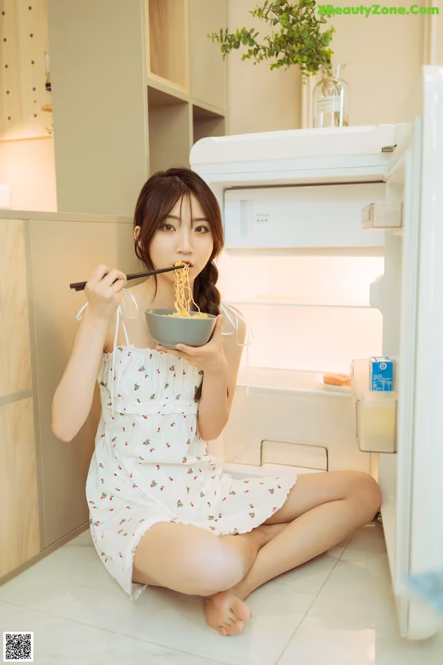 A woman sitting on the floor eating a bowl of noodles.