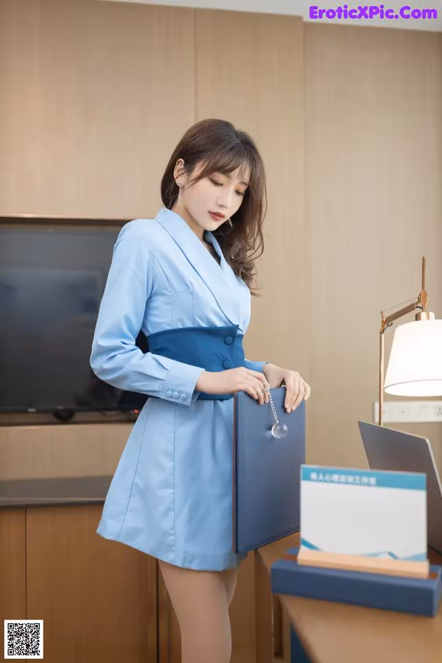A woman in a blue dress holding a blue folder.