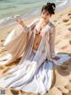 A woman in a white dress sitting on a beach.