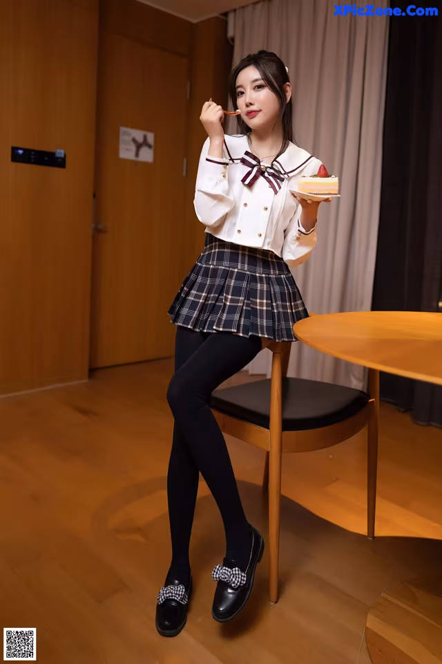 A woman in a school uniform holding a piece of cake.