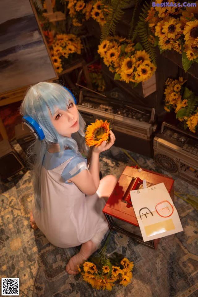 A woman with blue hair sitting on the floor holding a sunflower.