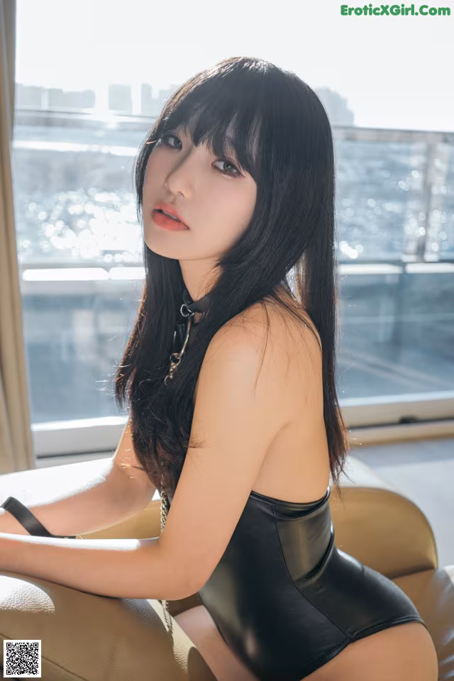 A woman in a black bodysuit sitting on a couch.