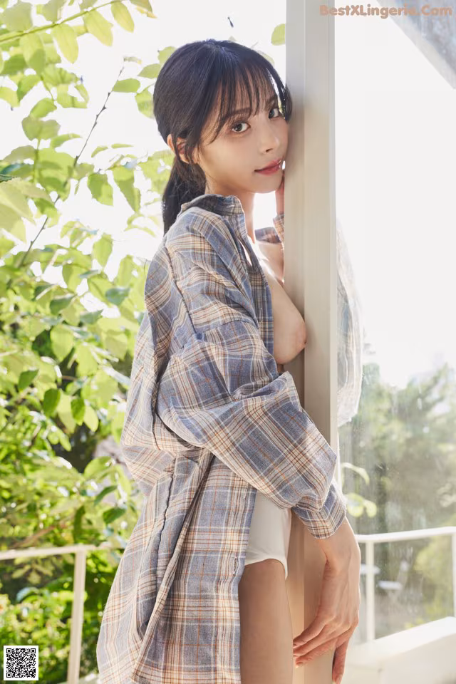 A woman in a plaid shirt leaning against a window.