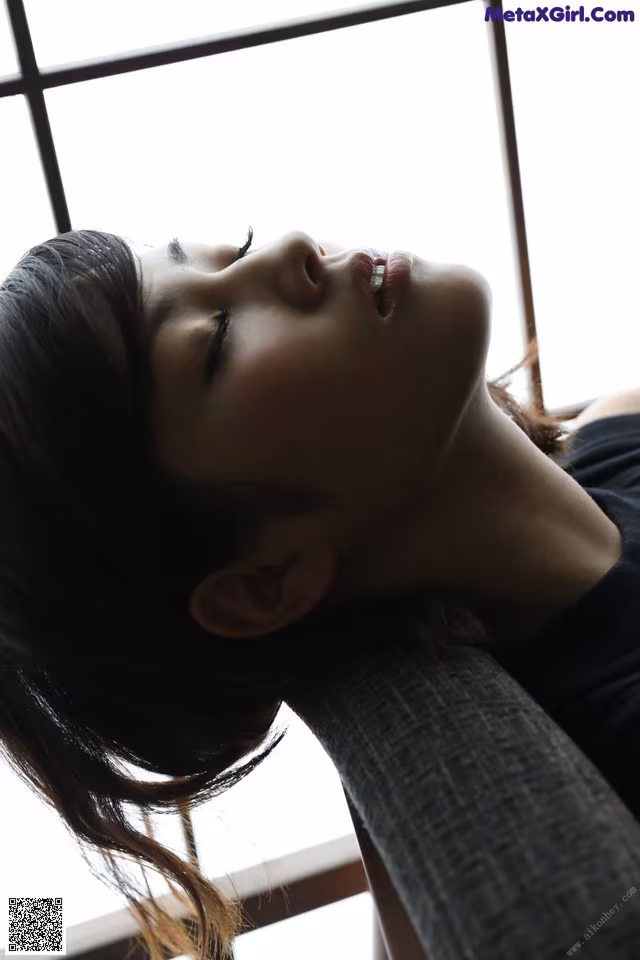 A woman leaning against a window with her eyes closed.