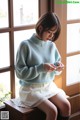 A woman sitting on a window sill looking at her phone.