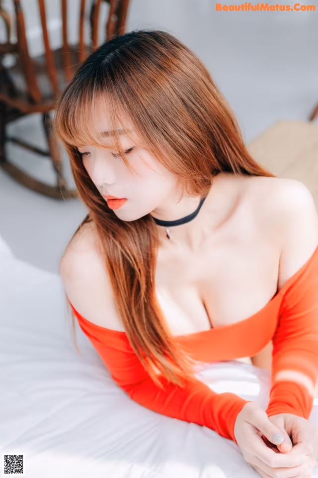 A woman in a red dress sitting on a bed.