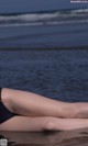 A woman in a black bathing suit laying on the beach.