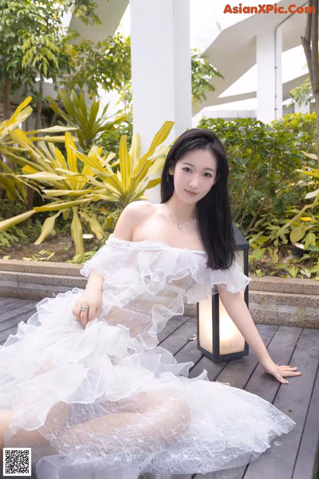 A woman in a white dress sitting on a wooden deck.