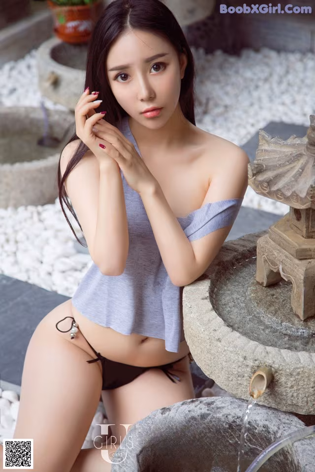 A woman in a gray top and black panties sitting next to a fountain.