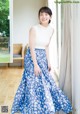 A woman standing in front of a window wearing a blue and white skirt.