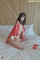 A woman in a red kimono sitting on a bed.