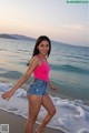 A woman in a pink tank top and denim shorts on the beach.