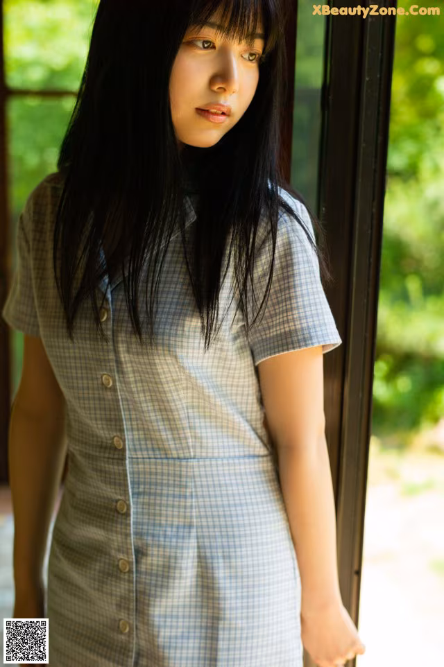 A woman standing in front of a window wearing a blue and white dress.