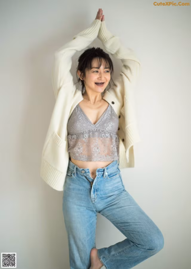 A woman in a white cardigan and jeans posing for a picture.