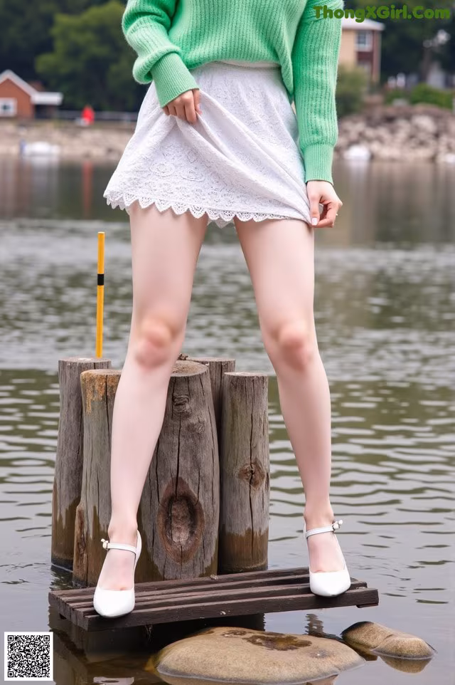 A woman in a green sweater and white skirt standing on a dock.