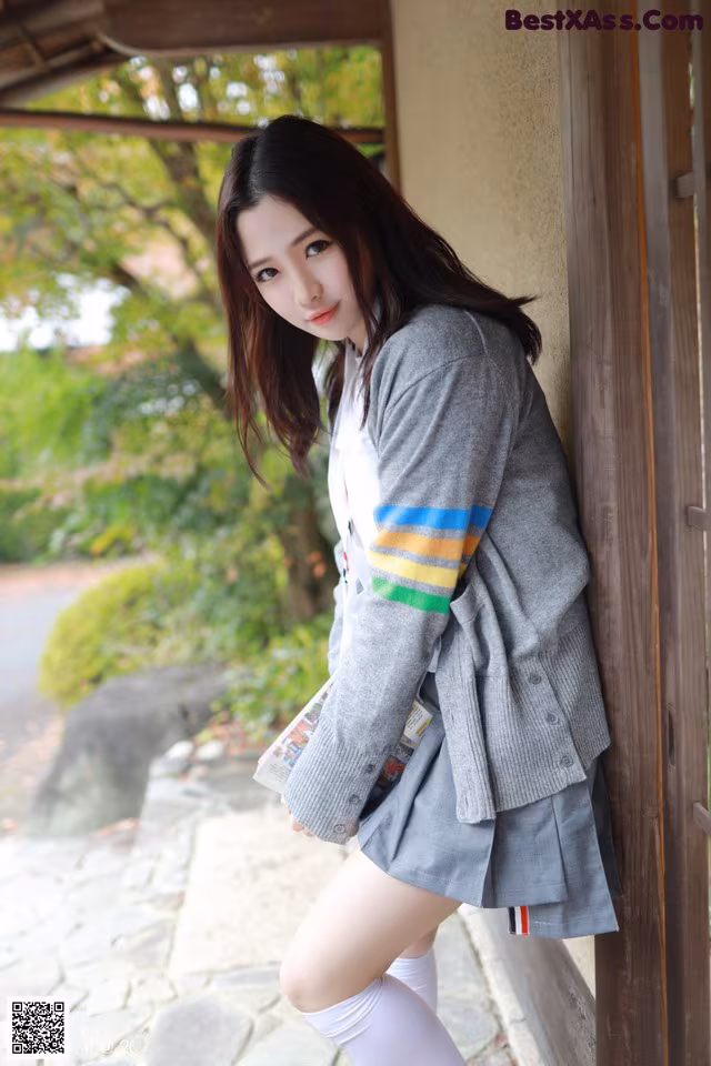 A woman in a school uniform leaning against a wall.