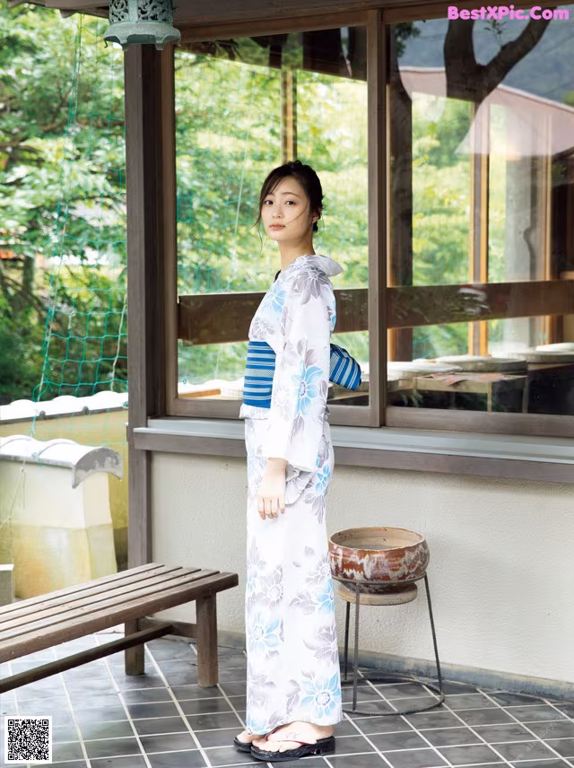 A woman in a kimono standing in front of a window.